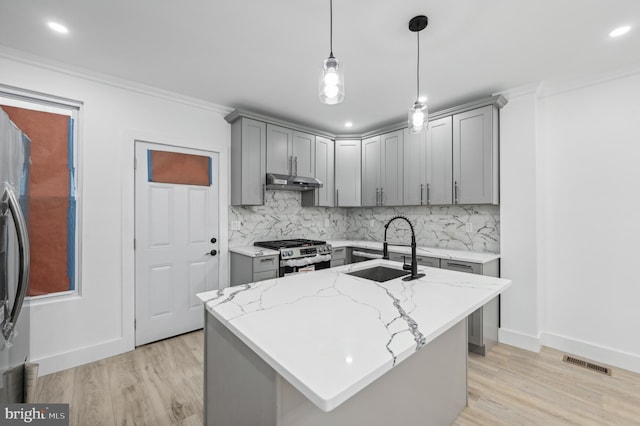 kitchen with sink, stainless steel range, light stone countertops, and an island with sink