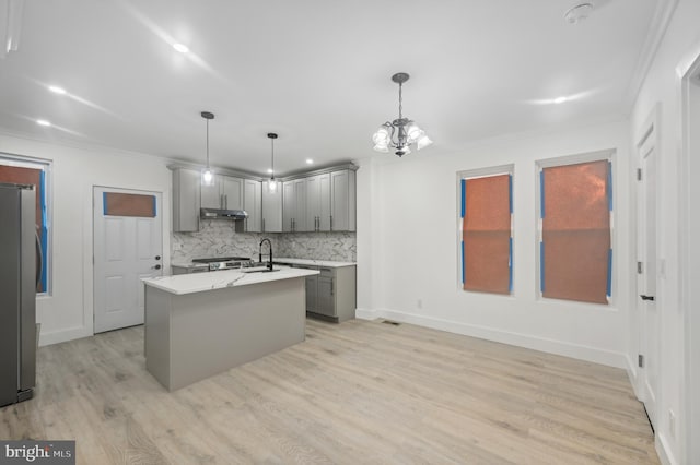 kitchen featuring a kitchen island with sink, hanging light fixtures, gray cabinetry, stainless steel appliances, and decorative backsplash