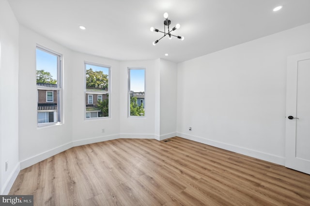 unfurnished room with a chandelier and light wood-type flooring