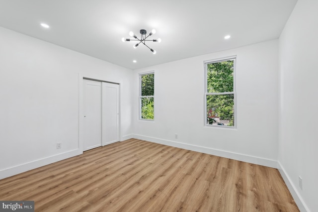 unfurnished bedroom with multiple windows, a notable chandelier, a closet, and light wood-type flooring