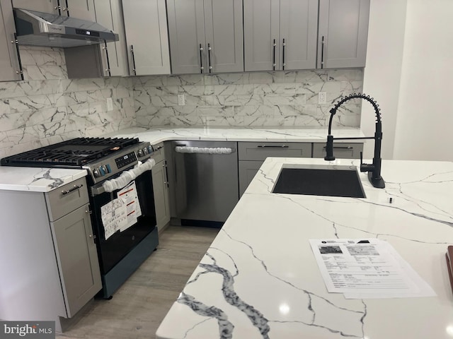 kitchen with light stone counters, tasteful backsplash, stainless steel appliances, and light hardwood / wood-style floors