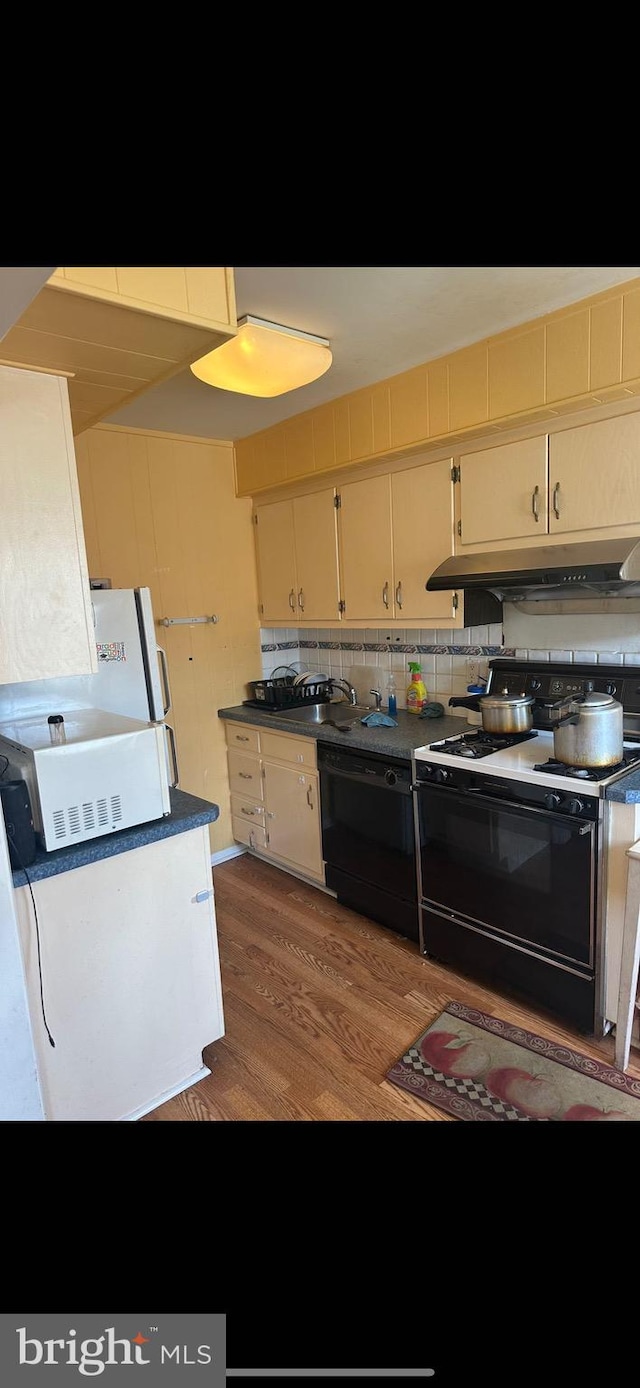 kitchen featuring cream cabinets, wood-type flooring, tasteful backsplash, white gas range oven, and dishwasher