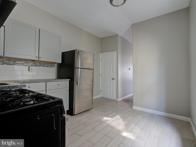 kitchen featuring decorative backsplash, white cabinets, light wood-type flooring, black range oven, and stainless steel fridge