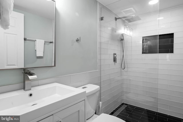 bathroom with vanity, tile walls, toilet, and tiled shower