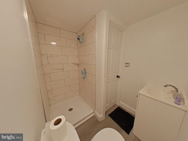 bathroom with a tile shower, vanity, hardwood / wood-style floors, and toilet