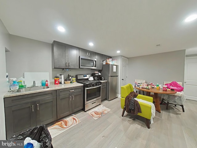 kitchen with light stone countertops, light hardwood / wood-style flooring, stainless steel appliances, and sink