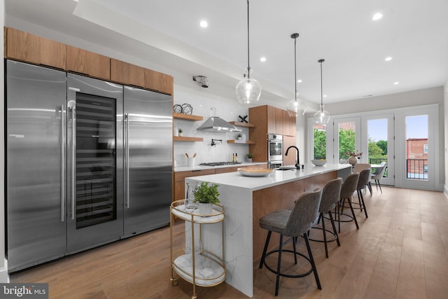 kitchen with stainless steel appliances, a breakfast bar, an island with sink, and exhaust hood