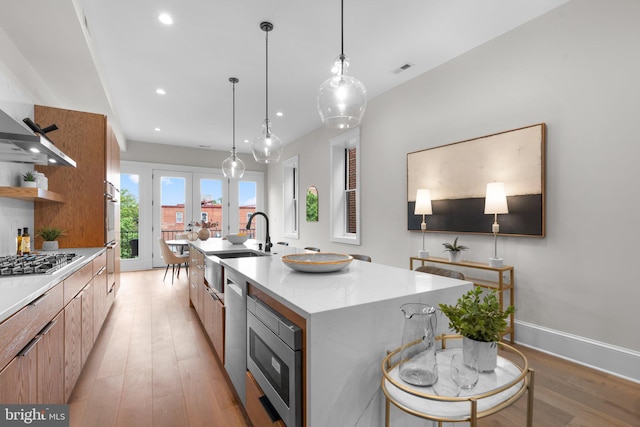 kitchen featuring appliances with stainless steel finishes, pendant lighting, a spacious island, sink, and light hardwood / wood-style flooring