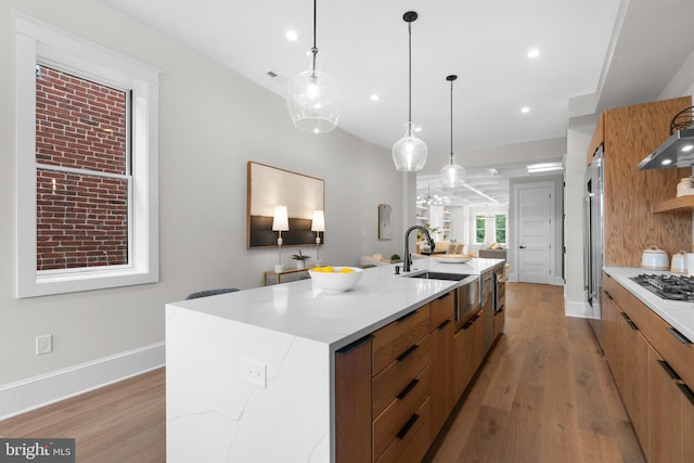 kitchen featuring a large island, pendant lighting, stainless steel appliances, light stone counters, and light wood-type flooring