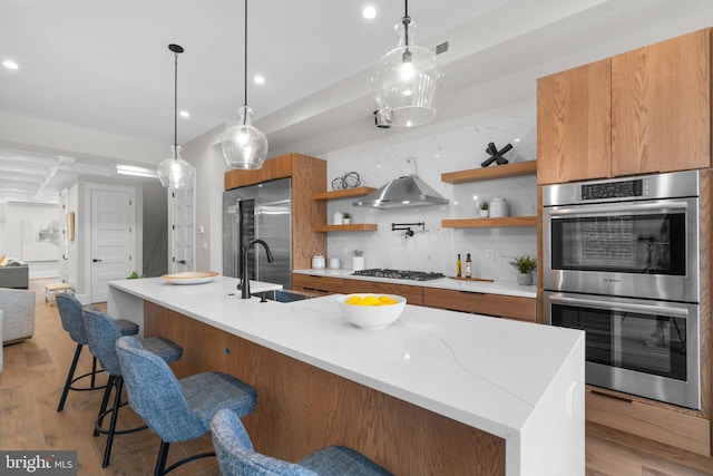 kitchen with sink, hanging light fixtures, stainless steel appliances, decorative backsplash, and light wood-type flooring