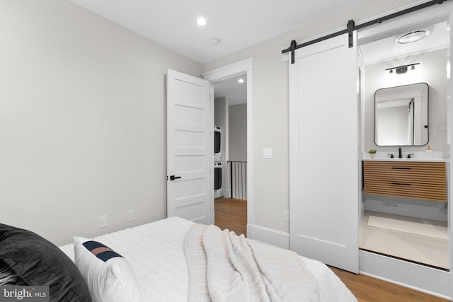 bedroom featuring wood-type flooring, a barn door, sink, and connected bathroom