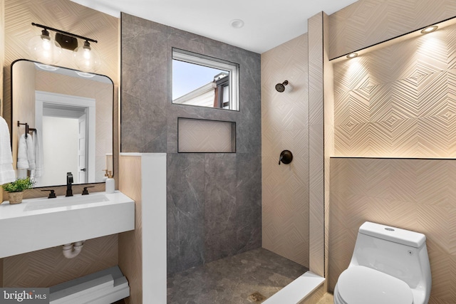 bathroom with tiled shower, toilet, sink, and tile walls