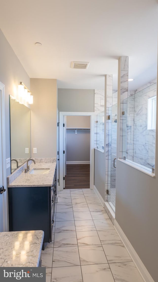 bathroom featuring vanity, visible vents, marble finish floor, a spacious closet, and a shower stall