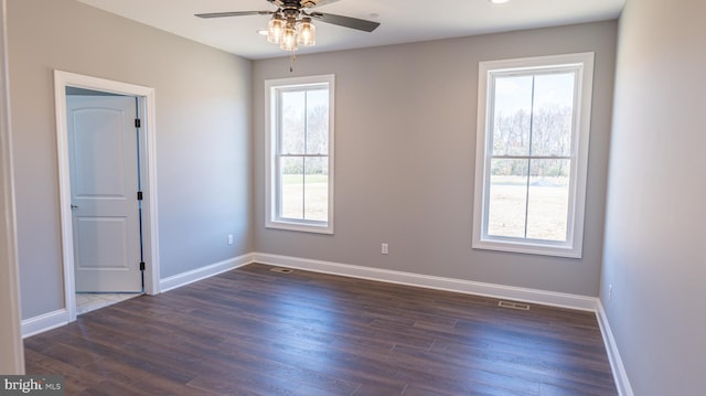 empty room with dark wood-style floors, visible vents, ceiling fan, and baseboards