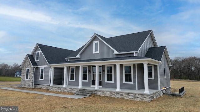 view of front of house featuring a shingled roof, a front yard, covered porch, and stone siding