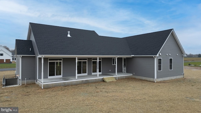 rear view of property featuring roof with shingles, a patio, and a lawn