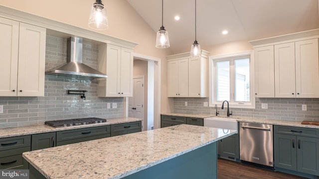 kitchen featuring stainless steel appliances, white cabinets, wall chimney range hood, a center island, and decorative light fixtures