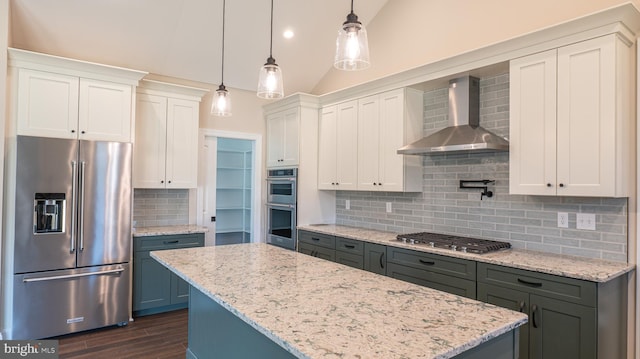 kitchen with decorative light fixtures, appliances with stainless steel finishes, white cabinets, vaulted ceiling, and wall chimney exhaust hood