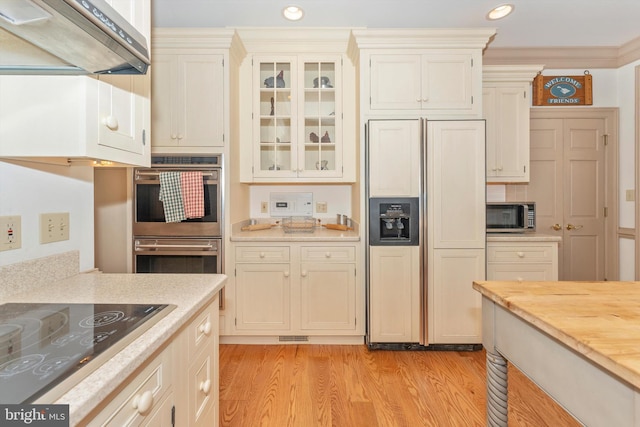 kitchen with ornamental molding, stainless steel appliances, light hardwood / wood-style floors, and wall chimney exhaust hood