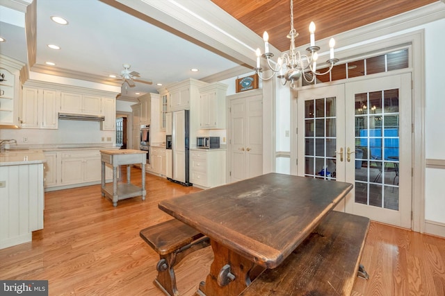 dining room with a tray ceiling, light hardwood / wood-style floors, ornamental molding, ceiling fan with notable chandelier, and french doors