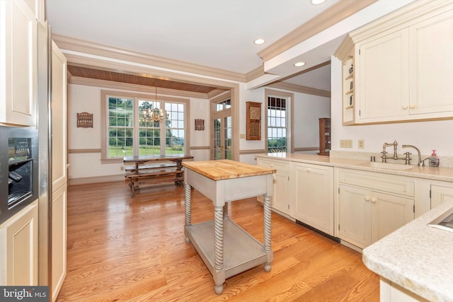 kitchen with pendant lighting, sink, cream cabinets, ornamental molding, and light hardwood / wood-style floors