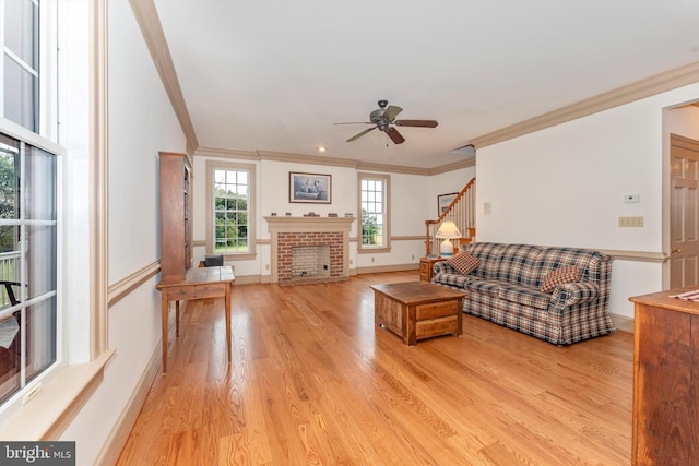 living room featuring ceiling fan, ornamental molding, a brick fireplace, and light wood-type flooring