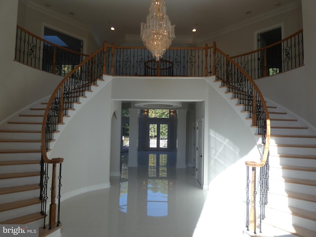 foyer entrance with a towering ceiling, ornamental molding, and a chandelier