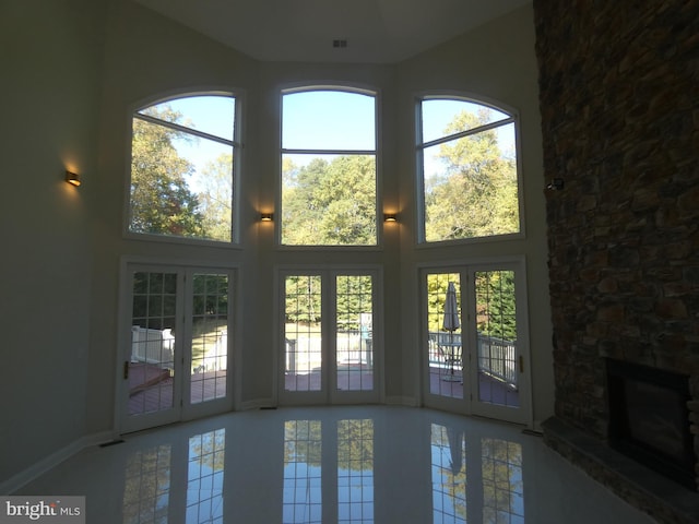 doorway to outside with a stone fireplace, a wealth of natural light, and a high ceiling