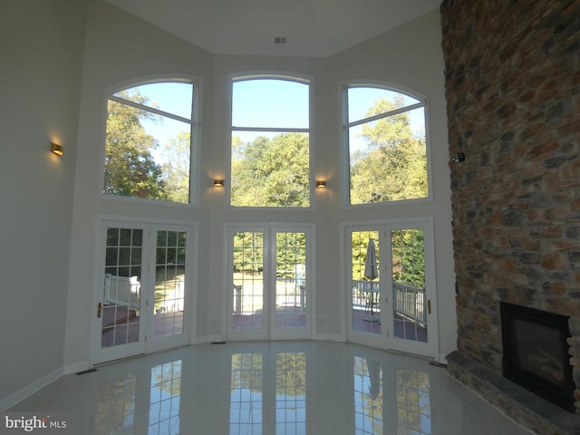 doorway featuring a towering ceiling, tile patterned floors, a stone fireplace, and a wealth of natural light