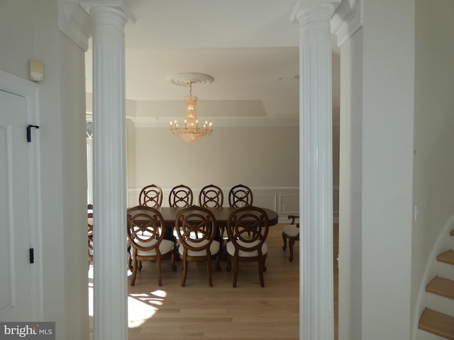 dining area with decorative columns, a tray ceiling, a chandelier, and light hardwood / wood-style flooring