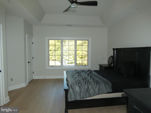 bedroom featuring a raised ceiling, ceiling fan, and light wood-type flooring