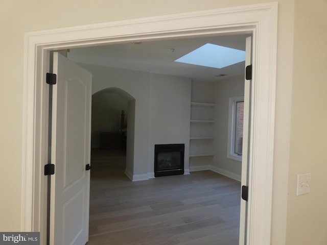 unfurnished living room with wood-type flooring, built in shelves, and a skylight