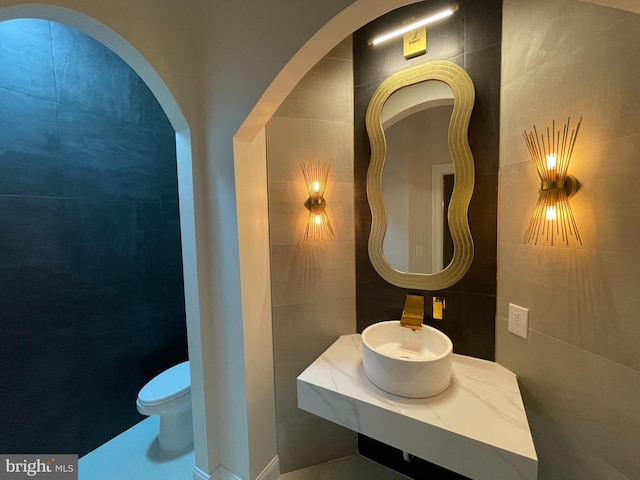 bathroom with sink, tile walls, and toilet