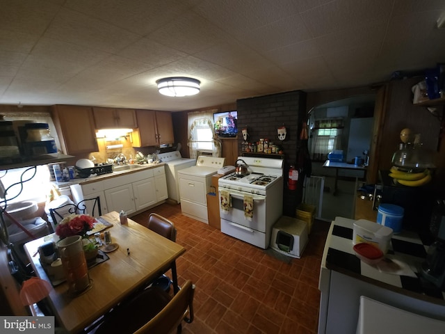 kitchen with sink, brick wall, white gas range, and independent washer and dryer