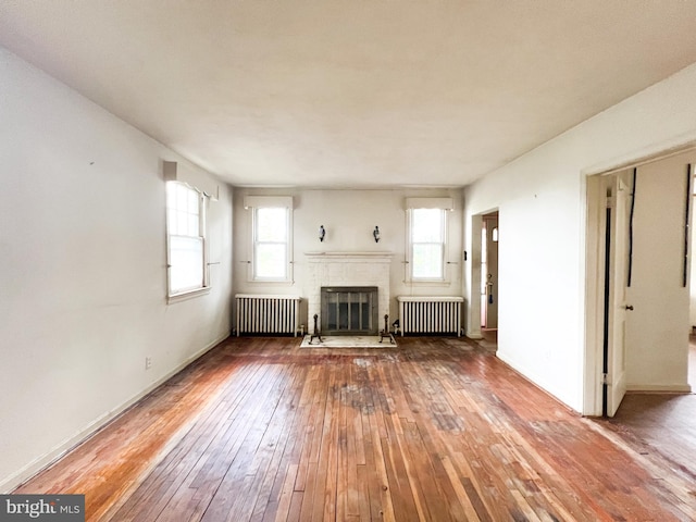 unfurnished living room featuring radiator, a brick fireplace, and hardwood / wood-style flooring