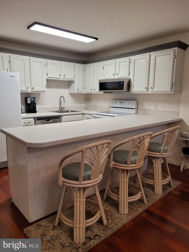 kitchen with white cabinets, sink, dark hardwood / wood-style floors, appliances with stainless steel finishes, and a kitchen breakfast bar