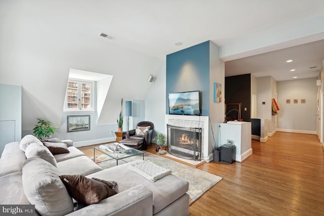 living room featuring recessed lighting, visible vents, wood finished floors, a warm lit fireplace, and baseboards