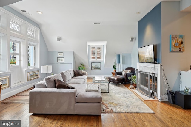 living area with lofted ceiling, visible vents, a lit fireplace, and wood finished floors