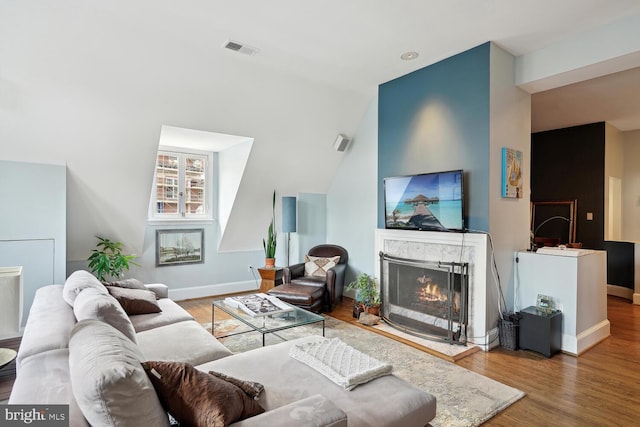 living room featuring visible vents, a fireplace, baseboards, and wood finished floors