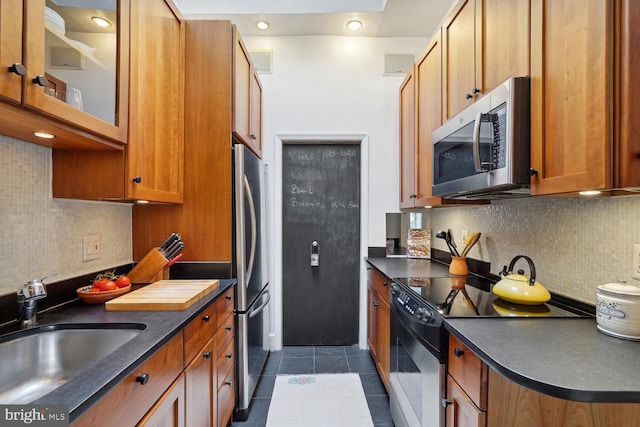 kitchen with dark tile patterned flooring, dark countertops, appliances with stainless steel finishes, a sink, and backsplash