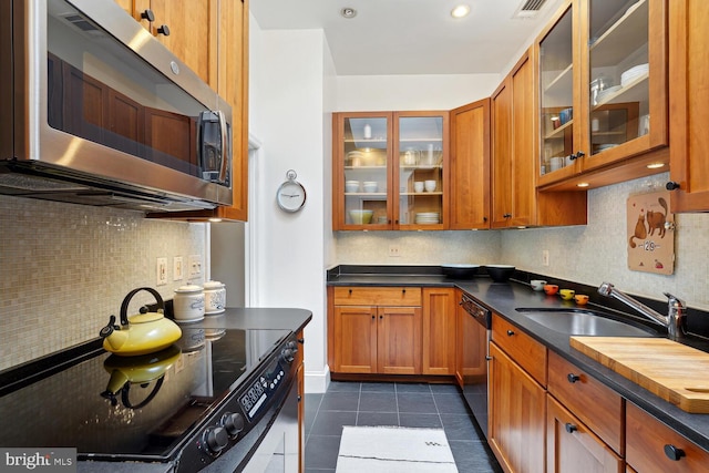 kitchen featuring appliances with stainless steel finishes, brown cabinets, a sink, and glass insert cabinets