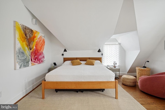 bedroom with vaulted ceiling, wood finished floors, and baseboards