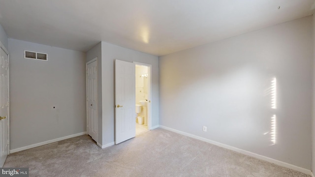 unfurnished bedroom with a closet, ensuite bathroom, and light colored carpet