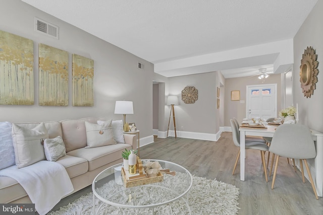 living room featuring ceiling fan, a textured ceiling, and light wood-type flooring