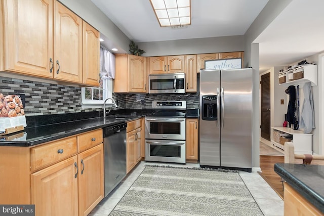 kitchen featuring sink, dark stone countertops, backsplash, stainless steel appliances, and light tile patterned flooring