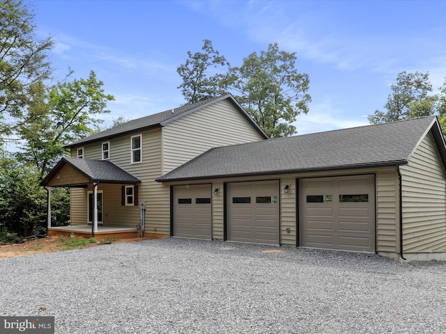 view of front facade with an attached garage, roof with shingles, a porch, and gravel driveway