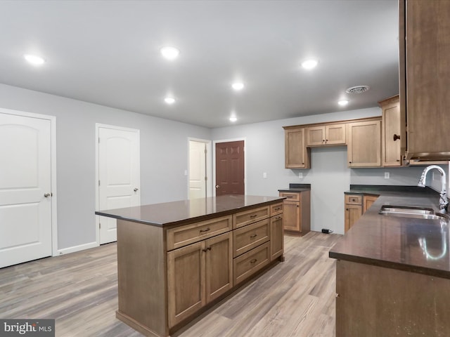 kitchen with a kitchen island, dark countertops, a sink, and light wood-style floors