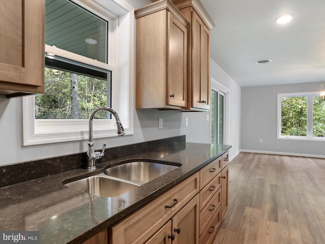 kitchen with visible vents, dark stone counters, brown cabinets, wood finished floors, and a sink