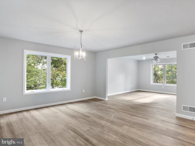 empty room with light wood-type flooring, baseboards, visible vents, and ceiling fan with notable chandelier