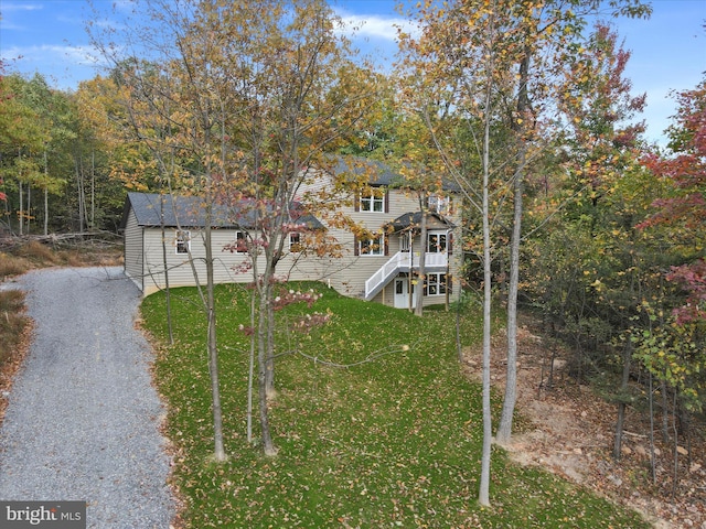 view of front facade with a front yard, gravel driveway, stairway, and a wooden deck